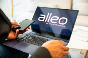 Utilisation d’un ordinateur portable affichant le logo Alleo de Bouygues Telecom, par une personne en tenue professionnelle tenant un téléphone